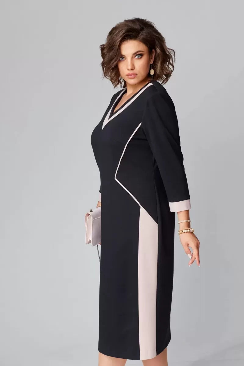 Model in black V-neck dress with beige accents, holding a clutch, facing sideways in a studio setting.