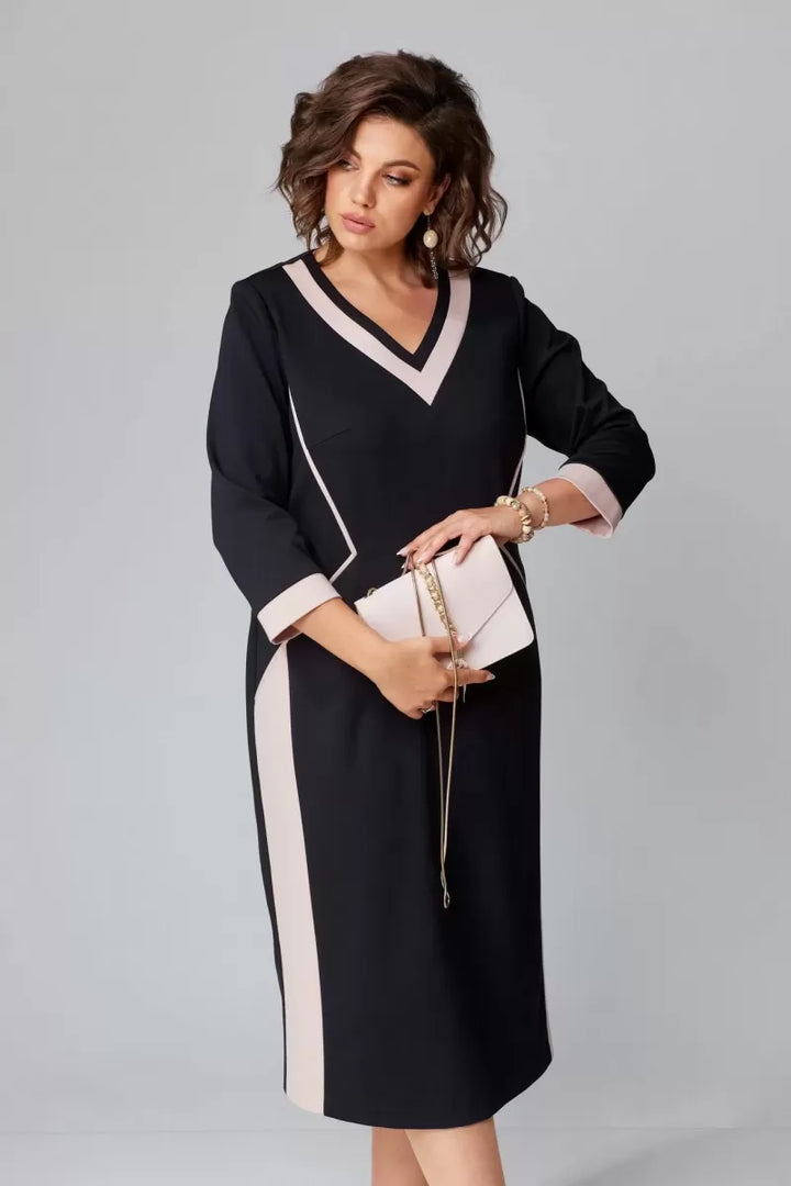 Model with wavy hair in a black and pink V-neck dress, holding a clutch in a studio setting.