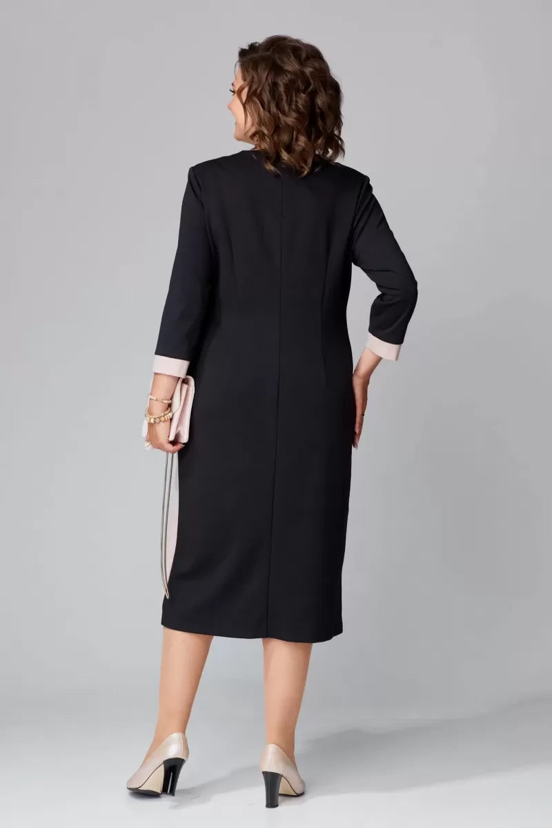 Back view of model in black V-neck dress with pink cuffs and a beige clutch in a studio.