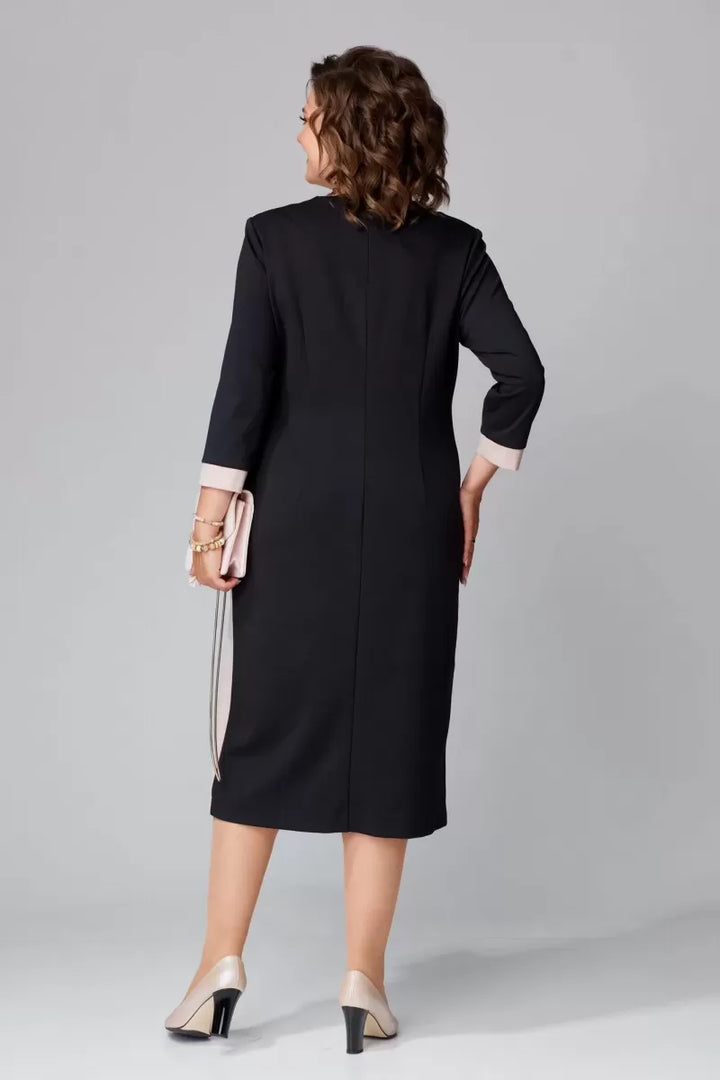 Back view of model in black V-neck dress with pink cuffs and a beige clutch in a studio.