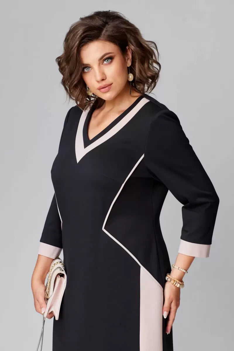 Model in elegant black and pink V-neck dress with accessorized jewelry, holding a clutch in a studio.