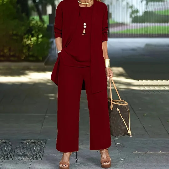 Red three-piece set featuring long jacket, top, and wide-leg pants. Outdoor walkway, woman holding a handbag.