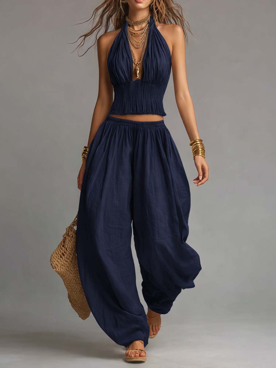 Navy two-piece set with a fitted halter top and loose pants, styled with gold accessories and a woven bag. Studio setting.