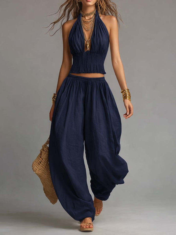 Navy two-piece set with a fitted halter top and loose pants, styled with gold accessories and a woven bag. Studio setting.