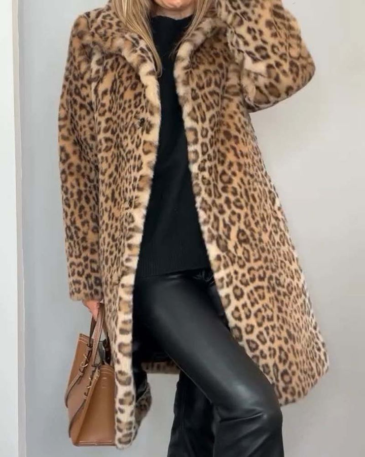 Woman wearing a leopard print coat in warm brown tones, paired with black outfit and brown handbag in a simple indoor setting.