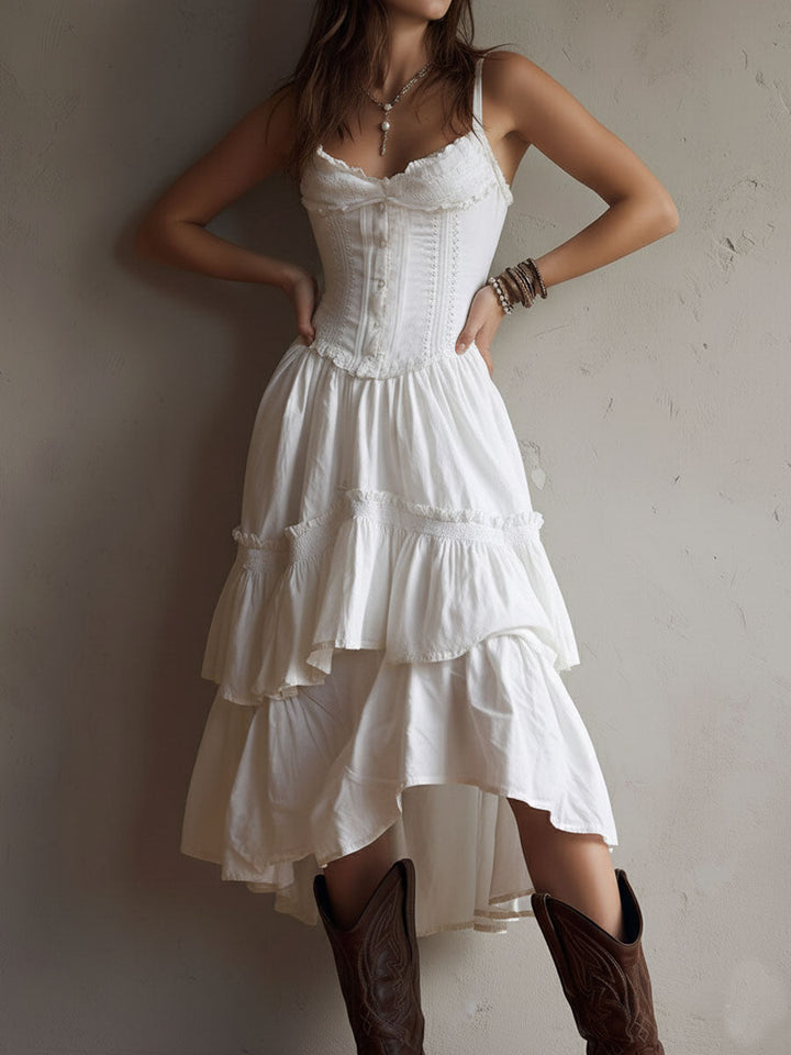 Woman wearing a white tiered midi dress, fitted bodice, brown boots. Neutral wall background.