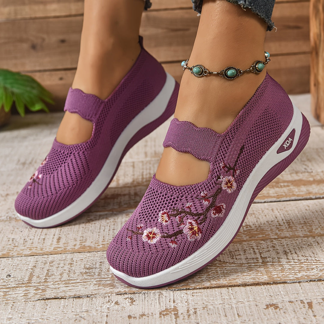 Purple orthopedic shoes with floral pattern, paired with anklet, on a textured wooden floor.