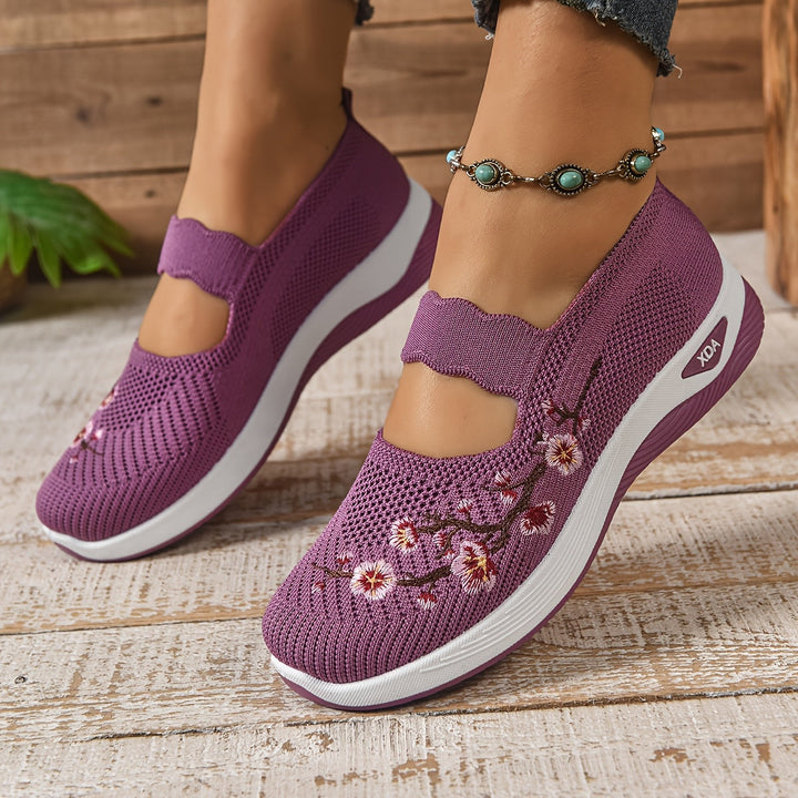 Purple orthopedic shoes with floral pattern, paired with anklet, on a textured wooden floor.