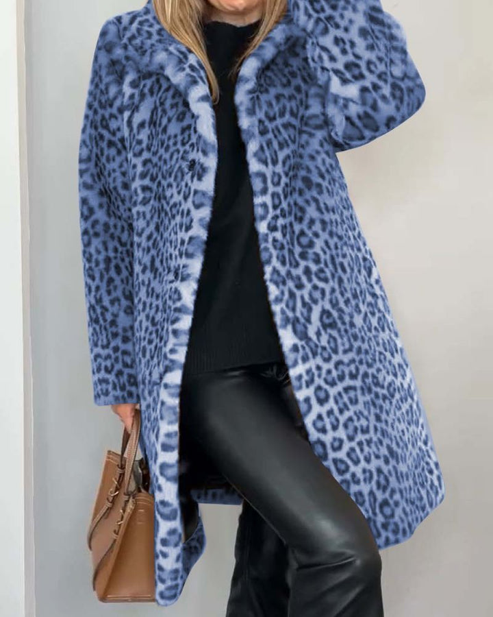 Woman dressed in a blue leopard print coat, accompanied by a black outfit and brown handbag, standing indoors.