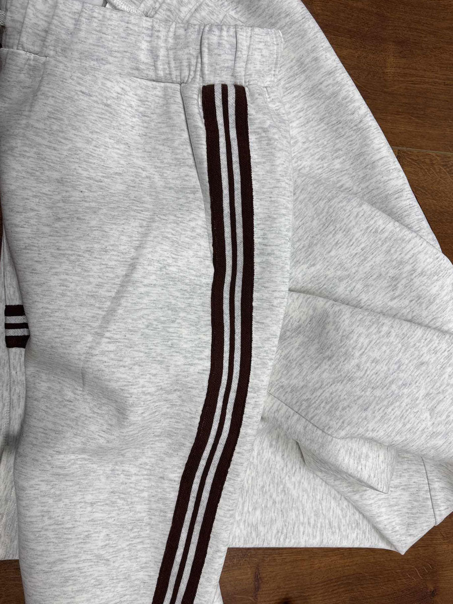 Close-up of light gray lounge pants with dark stripe on a wooden surface, showcasing the elastic waistband and piping details.