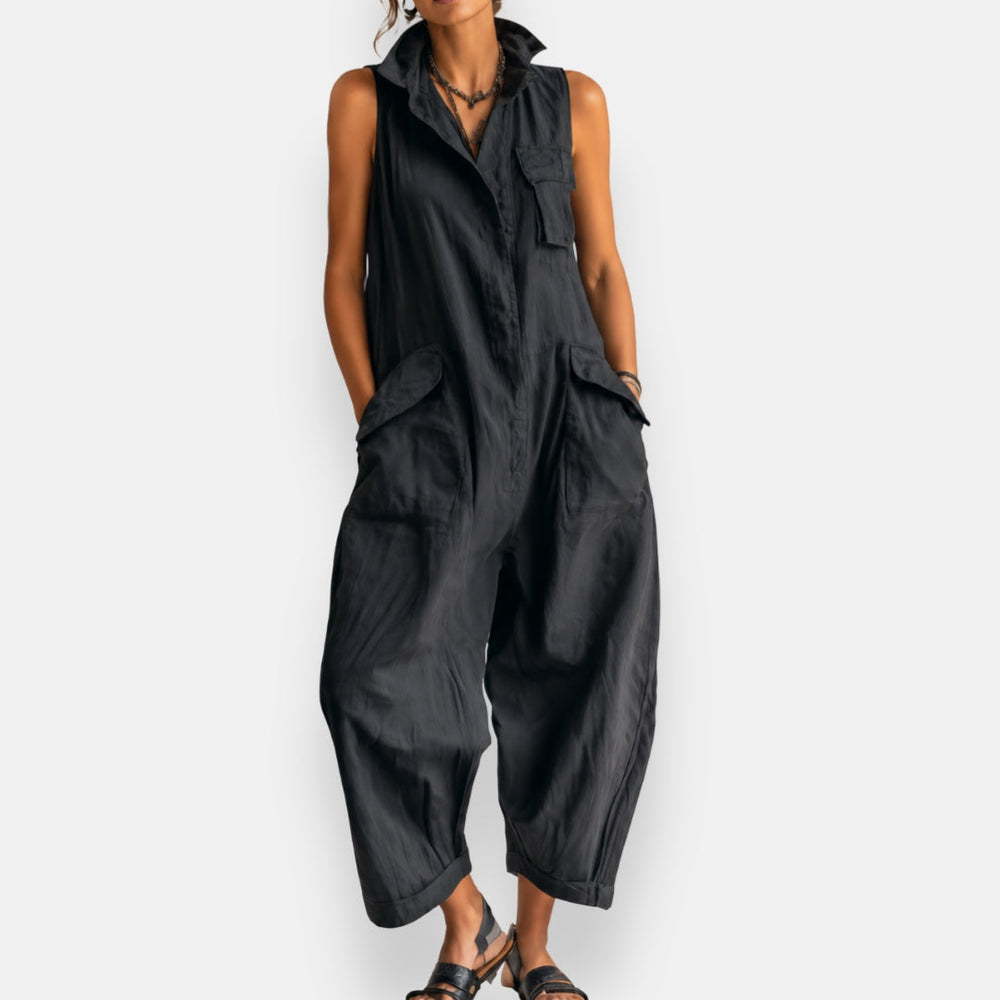 Navy sleeveless cargo jumpsuit with a casual fit, buttoned front, worn by a model standing in a studio setting.