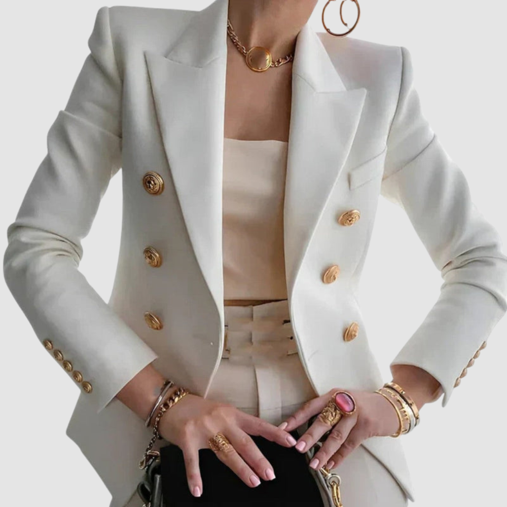 Sophisticated white blazer with gold buttons, worn over a cream outfit. Gold jewelry accessorizes the look in a studio setting.