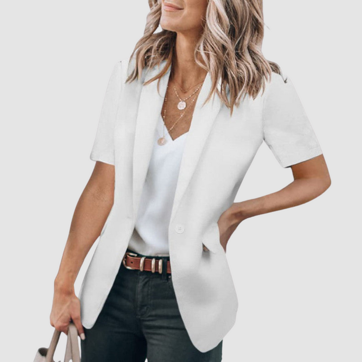 White short-sleeve blazer worn by person with wavy hair, white top, and jeans; holding a beige handbag against a plain background.