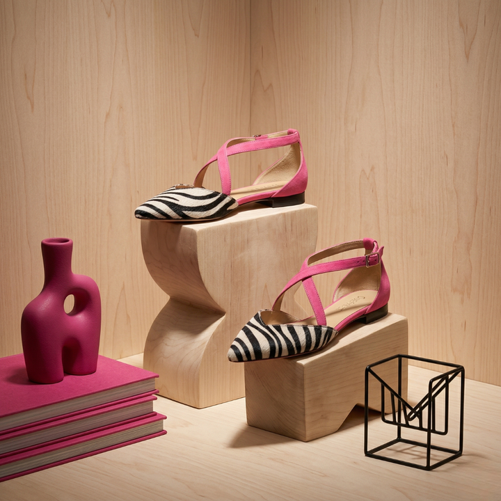 Pink zebra ballet flats displayed on wooden stands with vibrant decor in an indoor setting.