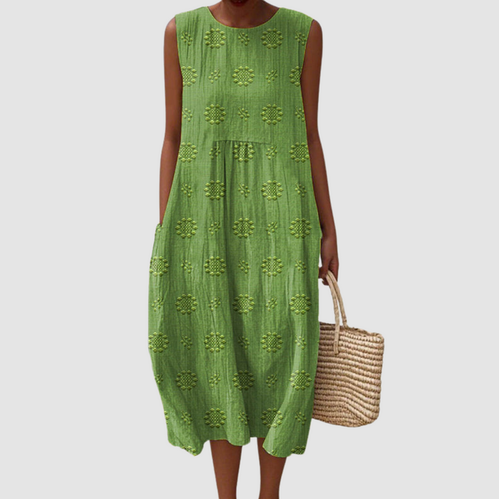 Green sleeveless summer dress with floral patterns, model holding a woven basket, white background.