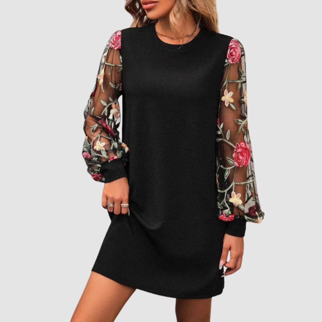 Black dress with floral lace long sleeves, worn by a woman. Studio background.