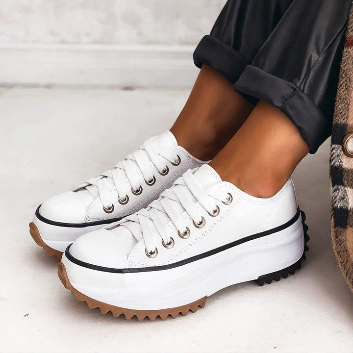 White platform shoes with thick white soles and white laces, worn with rolled-up black pants on a clean white floor.
