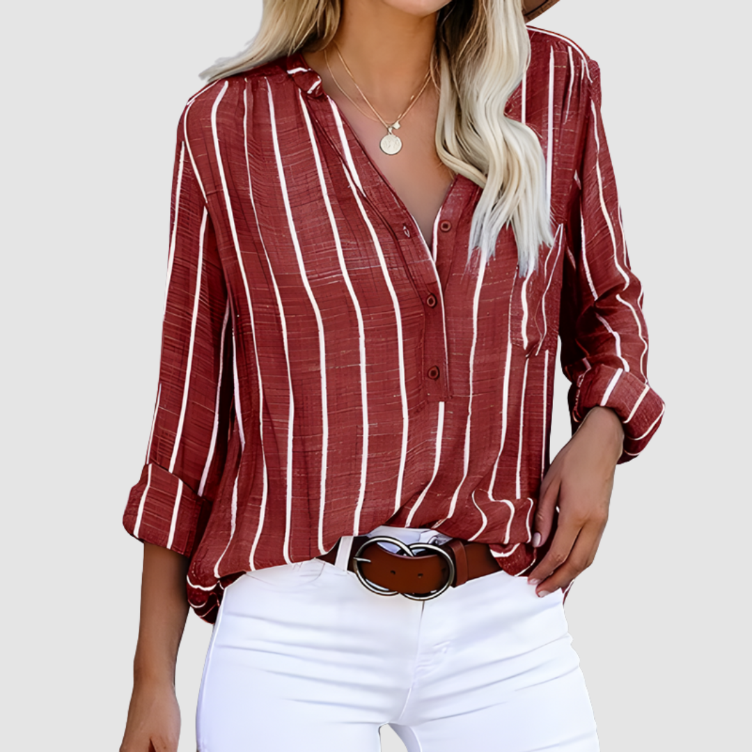 Red and white vertical striped blouse with rolled-up sleeves, styled with a belt and white pants. Studio setting.