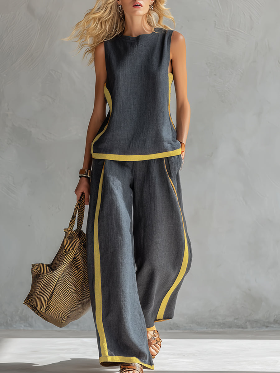 Model wearing a dark two-piece set with yellow trim, holding a straw bag, in a gray textured studio.