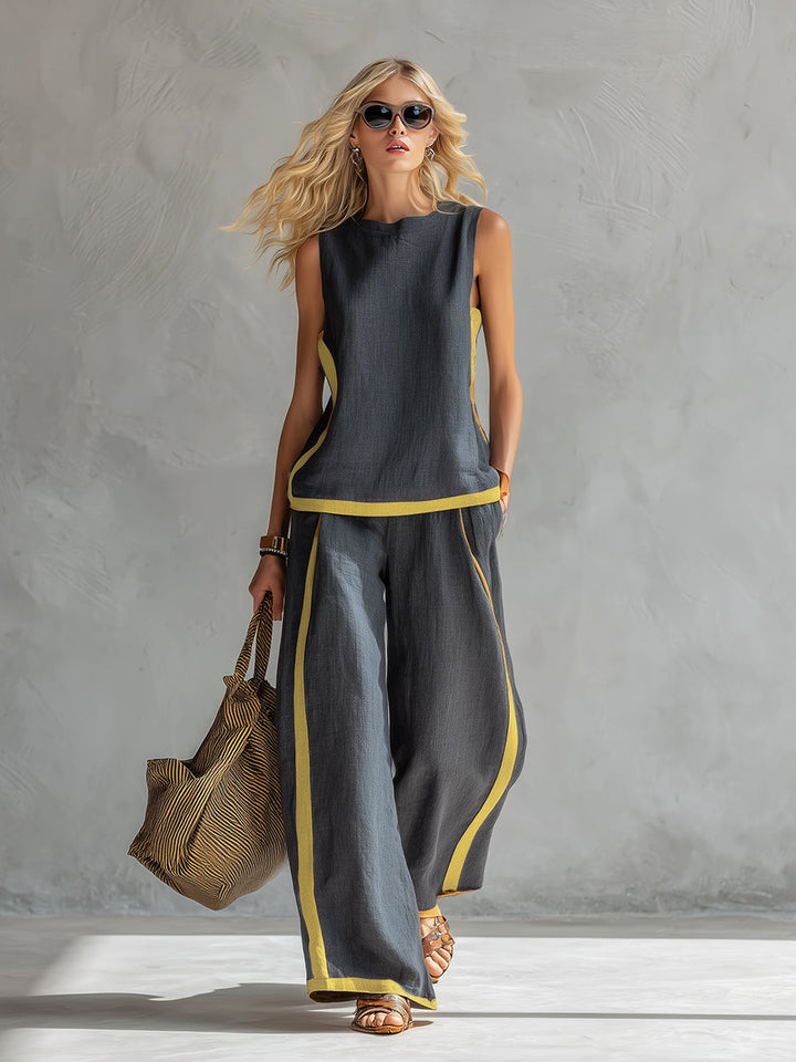 Model in a dark two-piece set with yellow trim, sunglasses, carrying a straw bag, set in a gray textured studio.
