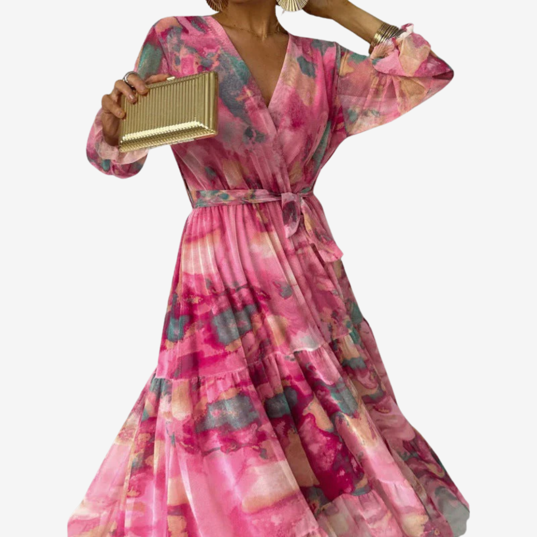 Close-up of elegant pink dress with long sleeves, abstract patterns, and a tied waist. Model holding a gold clutch, studio background.