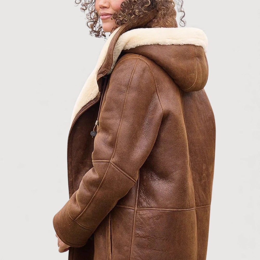 Side view of brown coat with hood and cream lining. Worn by a person. Light gray background.