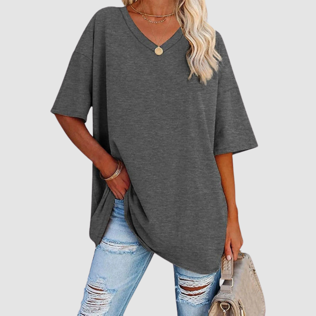 Woman in a gray V-neck T-shirt with distressed jeans, holding a beige bag, studio background.