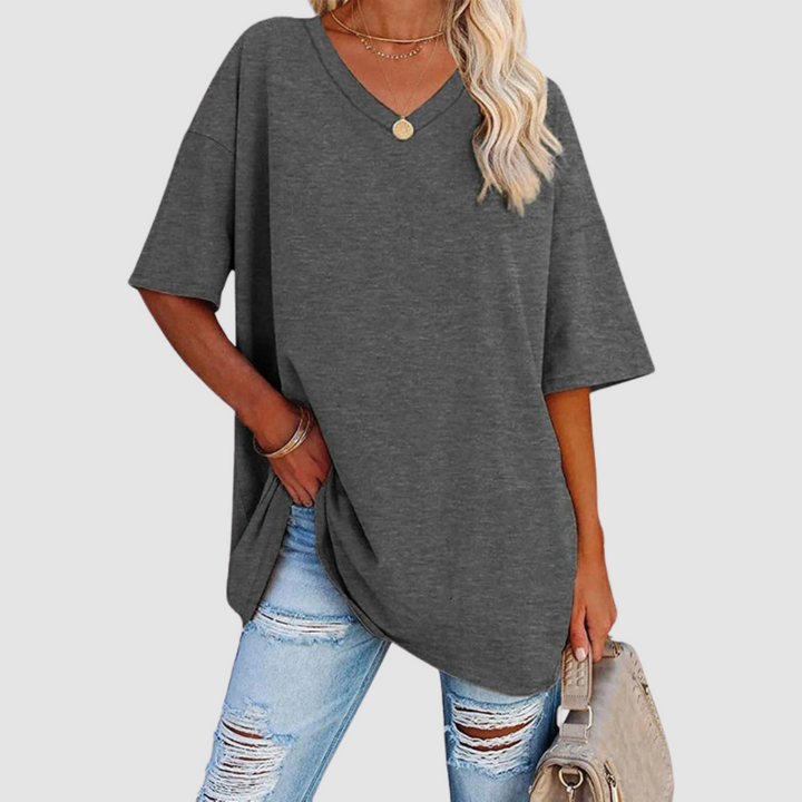 Woman in a gray V-neck T-shirt with distressed jeans, holding a beige bag, studio background.