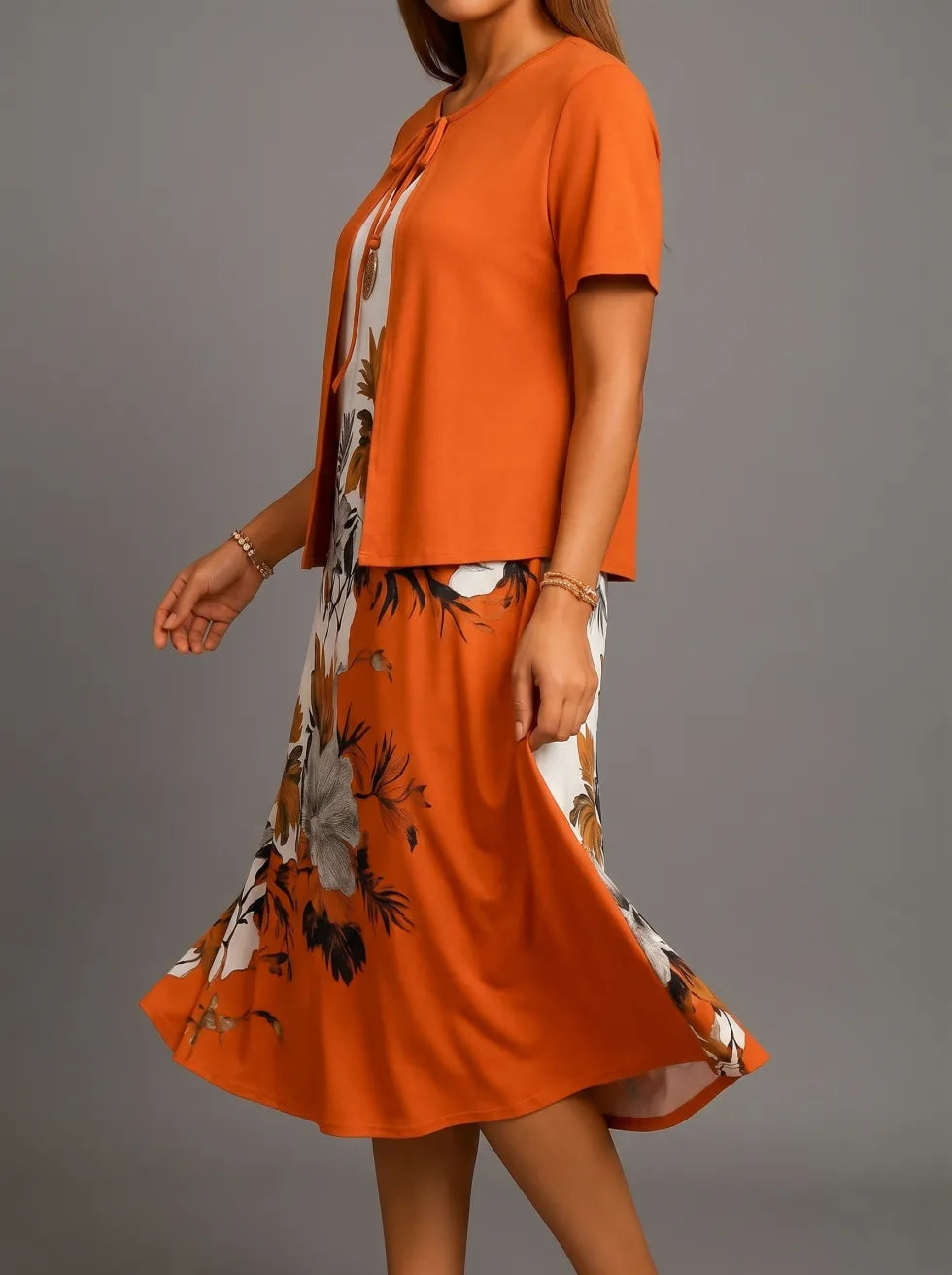 Side perspective of orange midi dress with floral pattern, featuring short sleeves and flowing design, studio backdrop.
