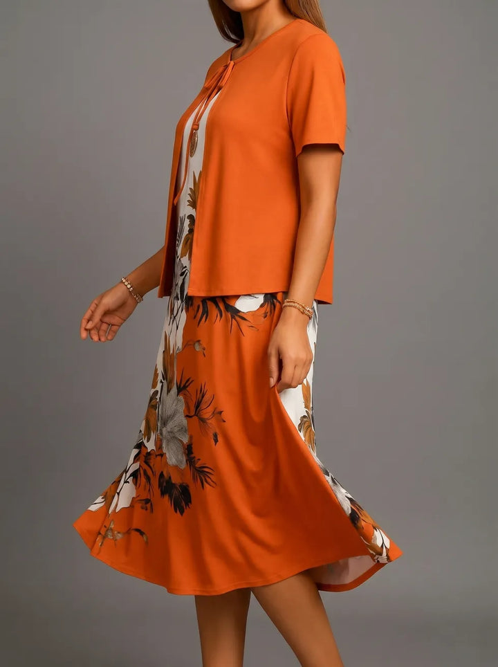Side perspective of orange midi dress with floral pattern, featuring short sleeves and flowing design, studio backdrop.