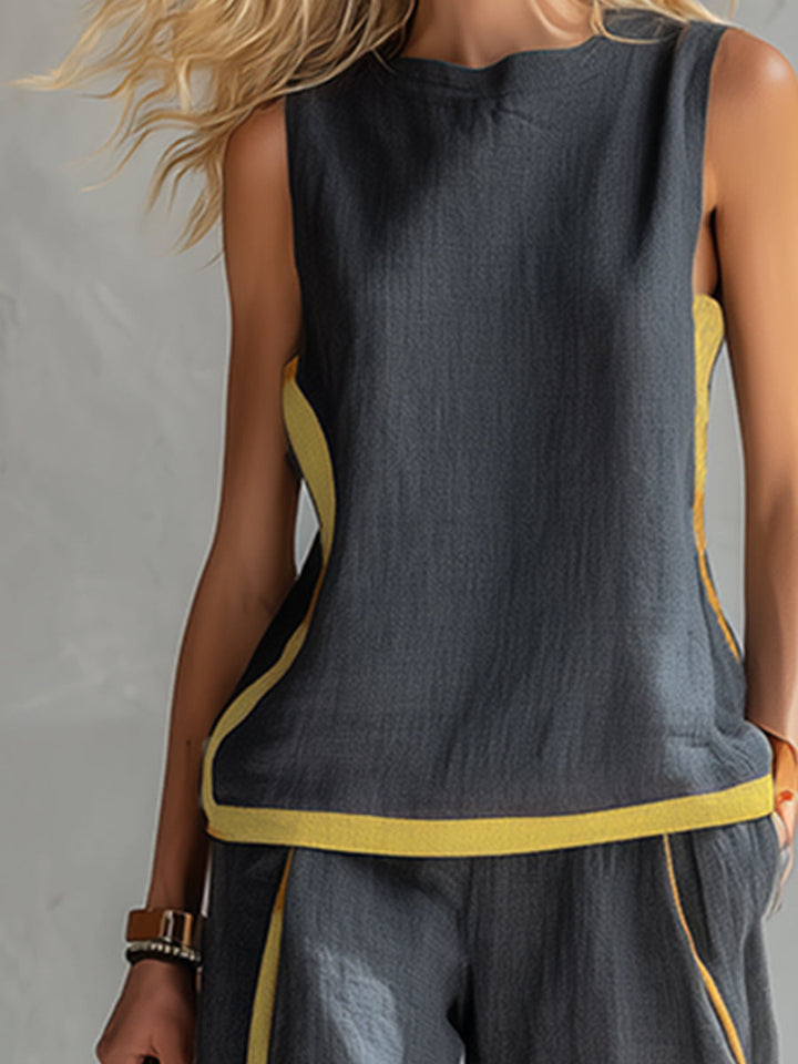 Close-up of dark sleeveless top with yellow sides and trim, worn by a model in a textured gray studio setting.