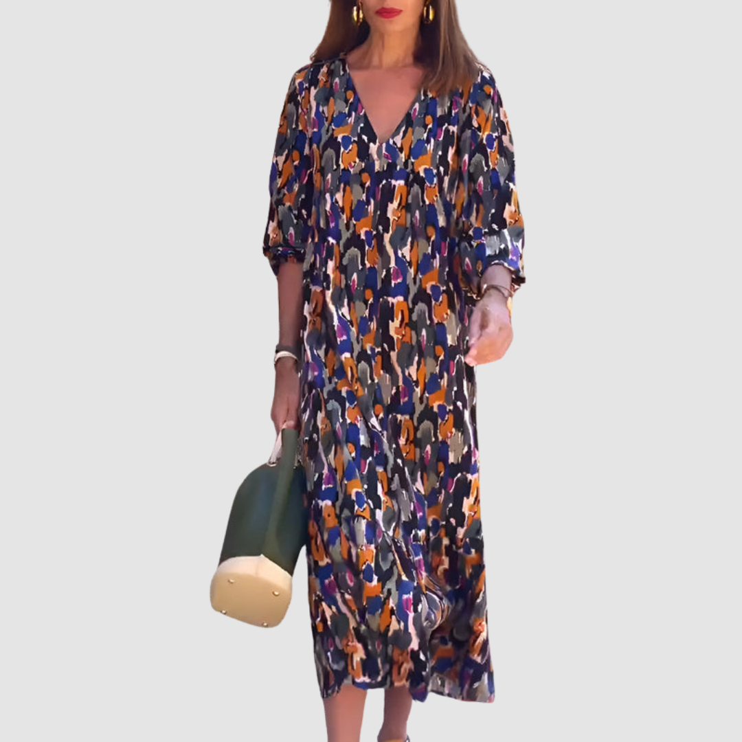 A woman wearing a colorful abstract print V-neck dress with three-quarter sleeves, carrying a green bag against a plain background.