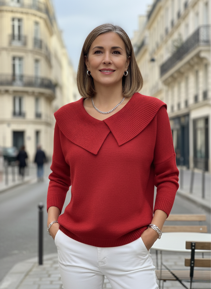 Woman in red elegant sweater with wide collar, standing on a European street, with historic buildings in the background.