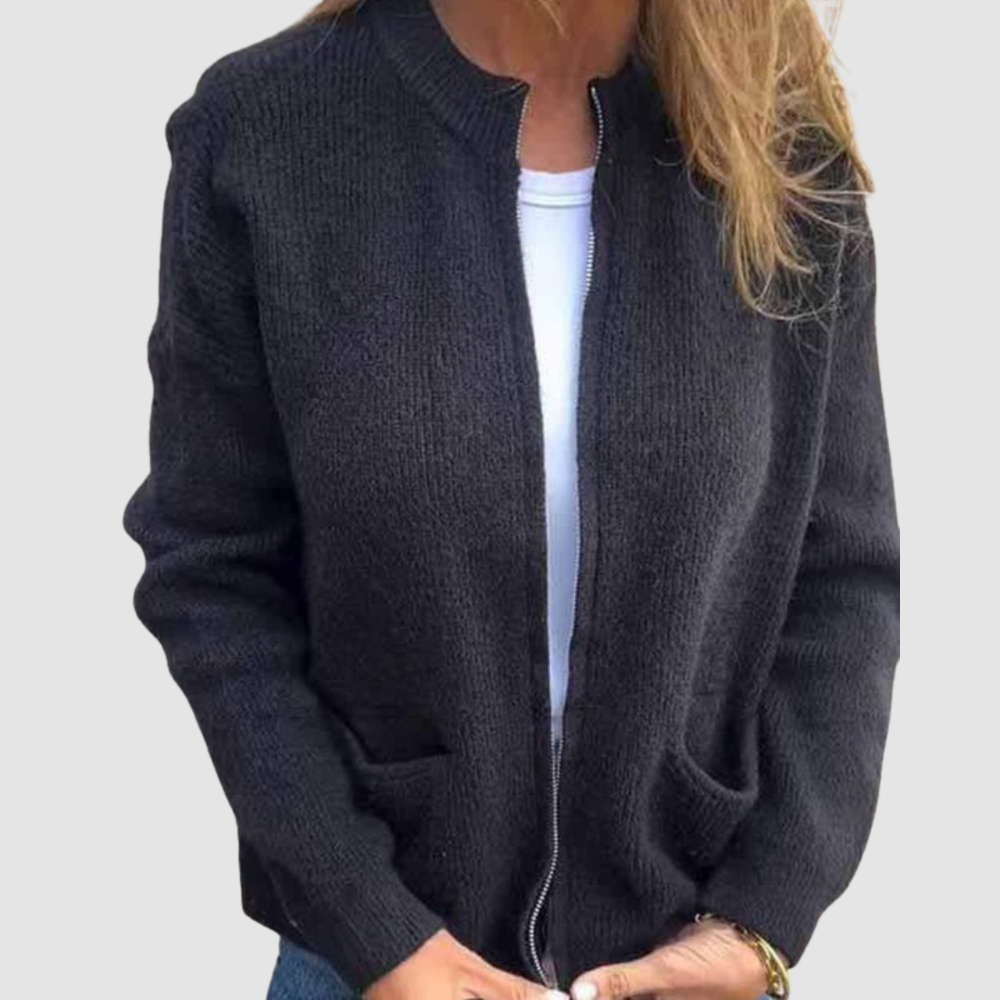 Black cozy cardigan worn over a white t-shirt with hands in pockets. Neutral background.