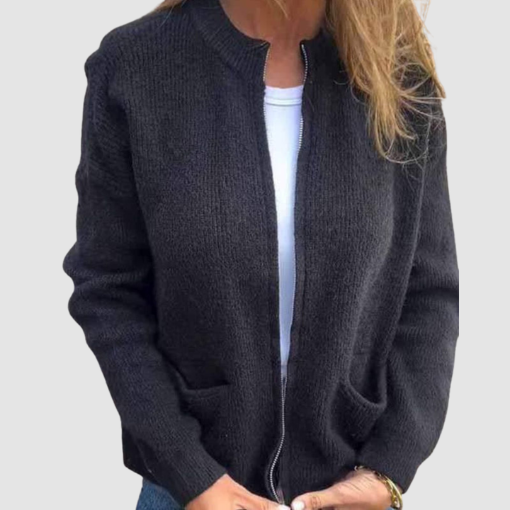 Black cozy cardigan worn over a white t-shirt with hands in pockets. Neutral background.