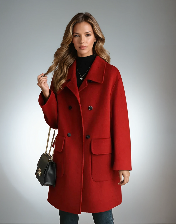 Vibrant red double-breasted coat with large pockets, worn over a black top, complemented by a small black handbag, studio setting.