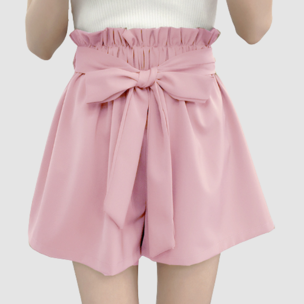 Pink paperbag waist shorts with a bow, paired with a white top in a studio background.