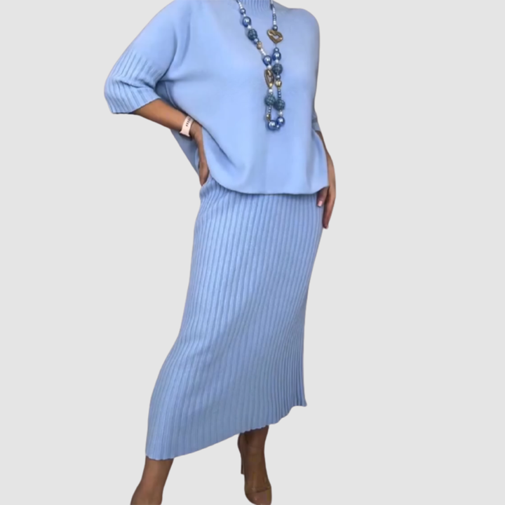 Side view of light blue 2-piece set, ribbed skirt and loose top with heart-themed necklace on plain background.