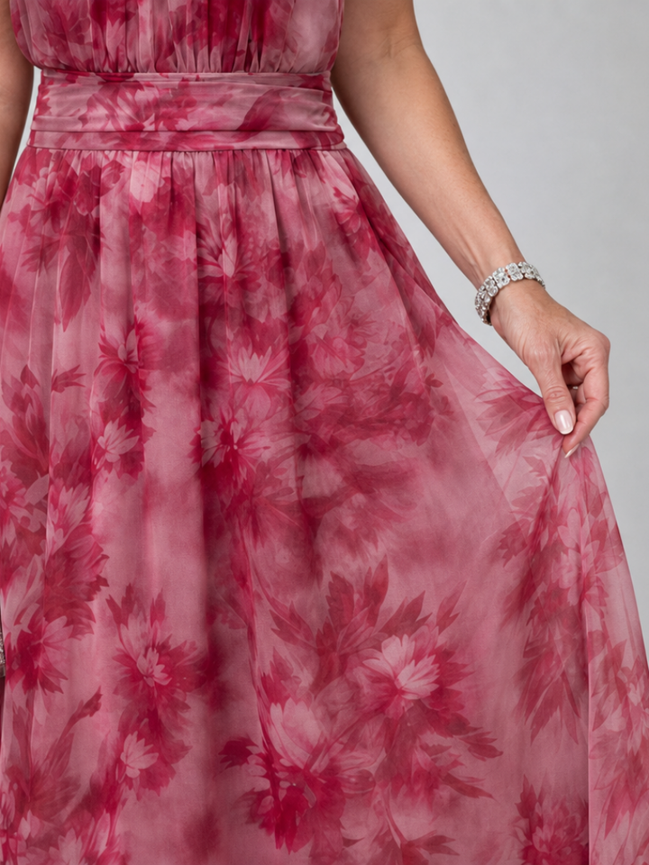 Close-up of pink floral halter neck midi dress fabric, woman gently holding skirt, studio background.