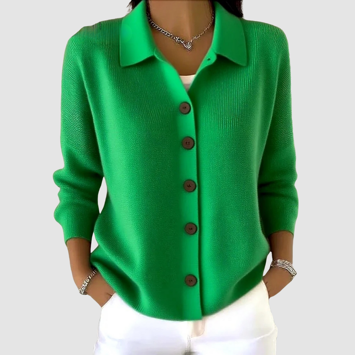 Bright green button-up knit cardigan with brown buttons, worn with white pants in a studio setting.