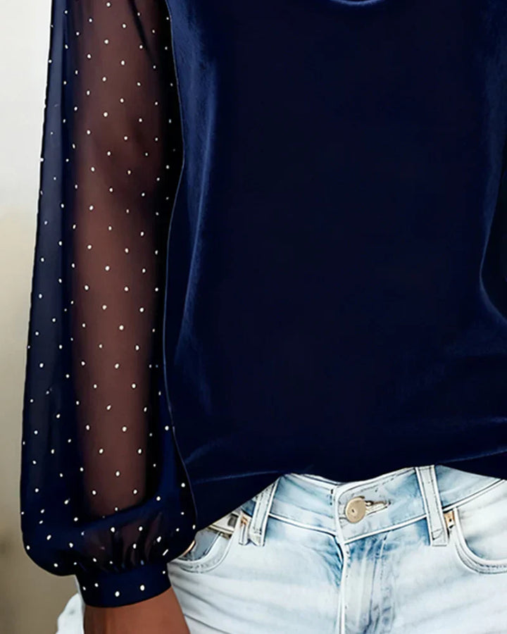 Close-up of navy blue blouse with sheer polka dot sleeve and light denim jeans in bright indoor setting.