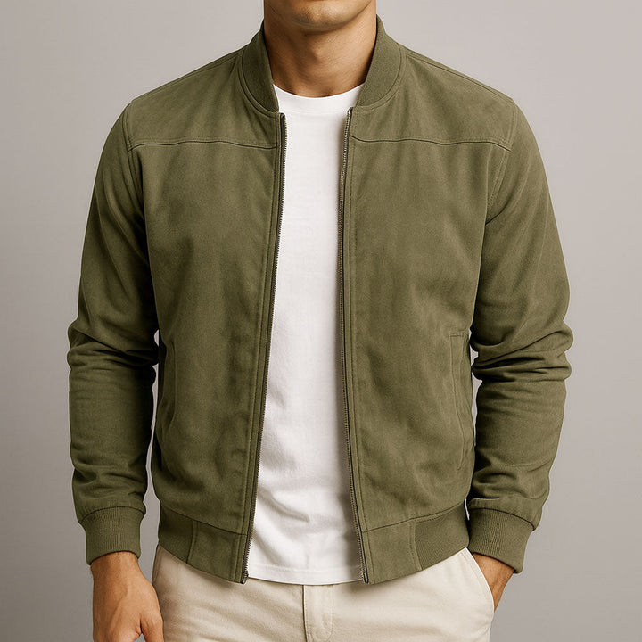 Man wearing an olive urban classic jacket, white shirt, and beige pants in a studio setting.