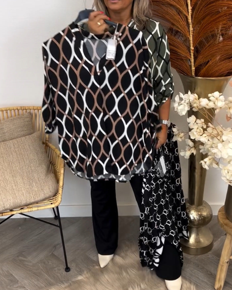 Person showcasing brown graphic print blouse while wearing a green print top with decor elements like florals and wicker chair.
