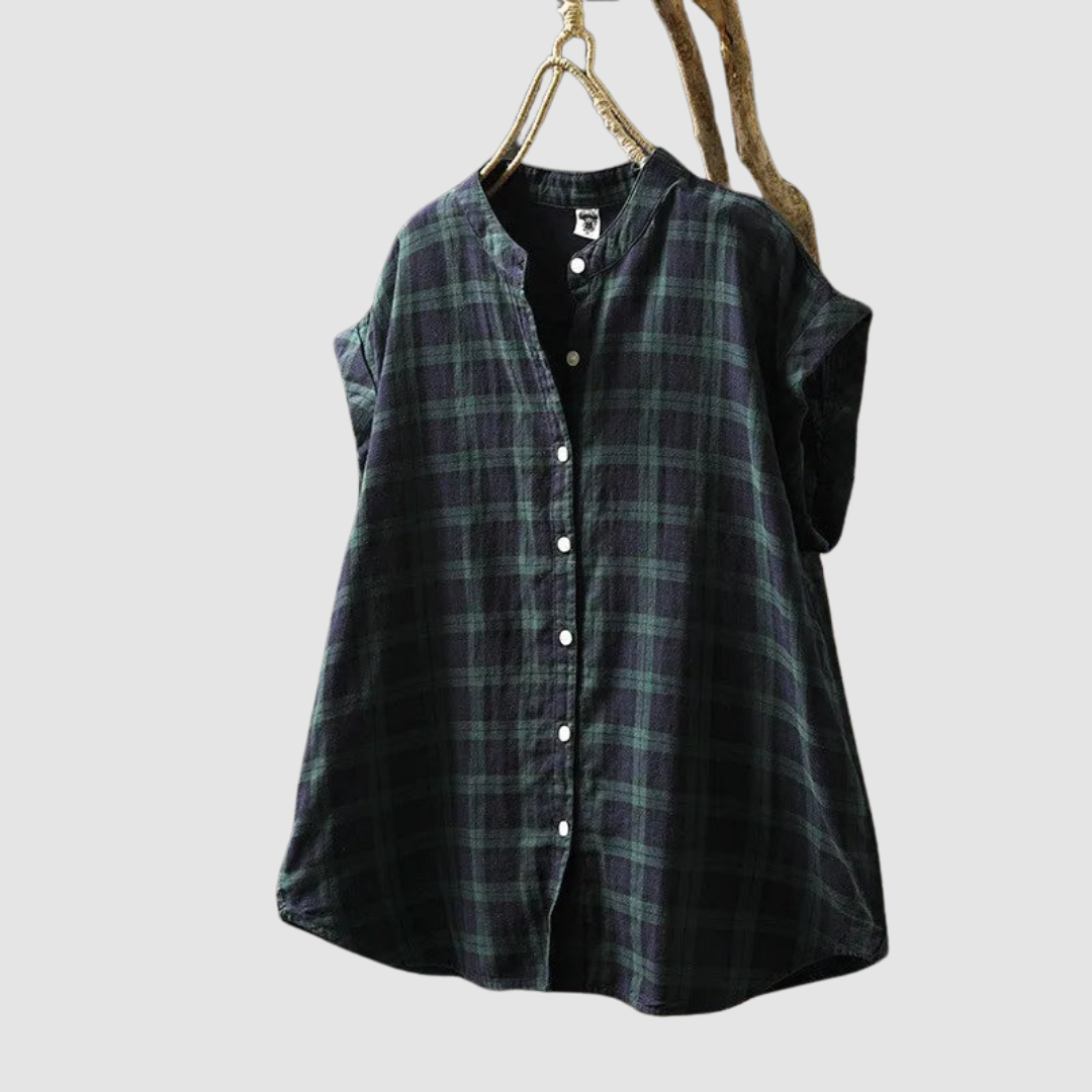 Dark plaid vintage shirt with short sleeves and buttons, hanging on a rustic branch against a gray background.