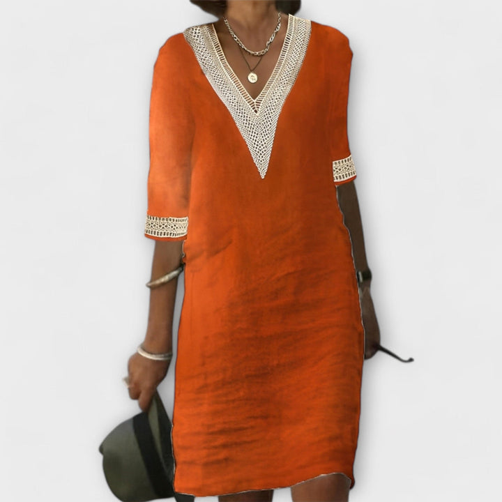Orange elegant dress featuring V-neck and lace trim, accessorized with silver jewelry on a plain backdrop.