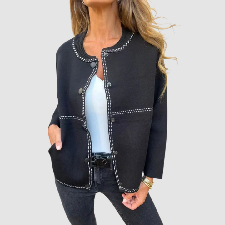Black jacket with round collar, button closure, worn over white top and black jeans in a studio setting.