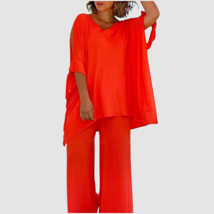 Woman in a bold orange relaxed style set with a loose top and wide-leg pants, set against a minimal backdrop.