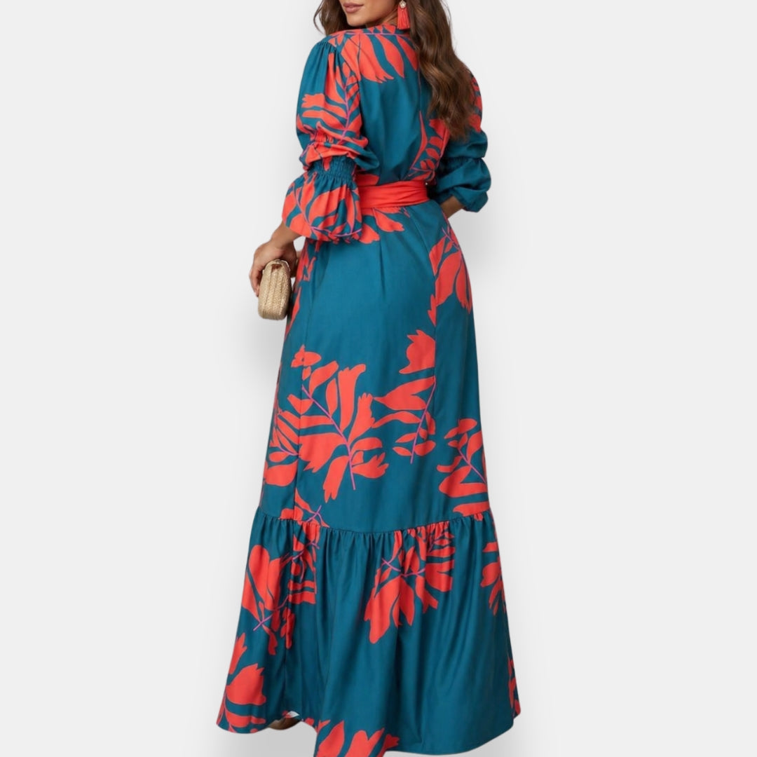 Back view of a teal maxi dress featuring red tropical floral patterns and a cinched waist, worn in a studio setting.