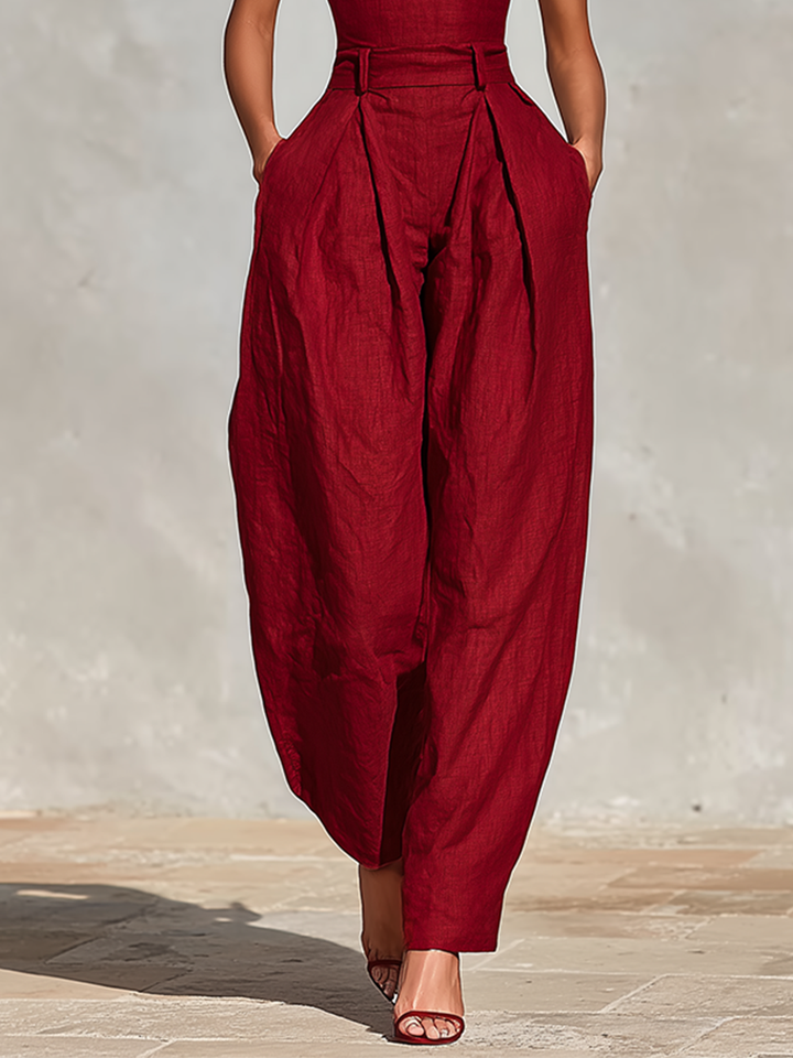 Lower half view of deep red jumpsuit with wide legs, on a sunlit stone floor.
