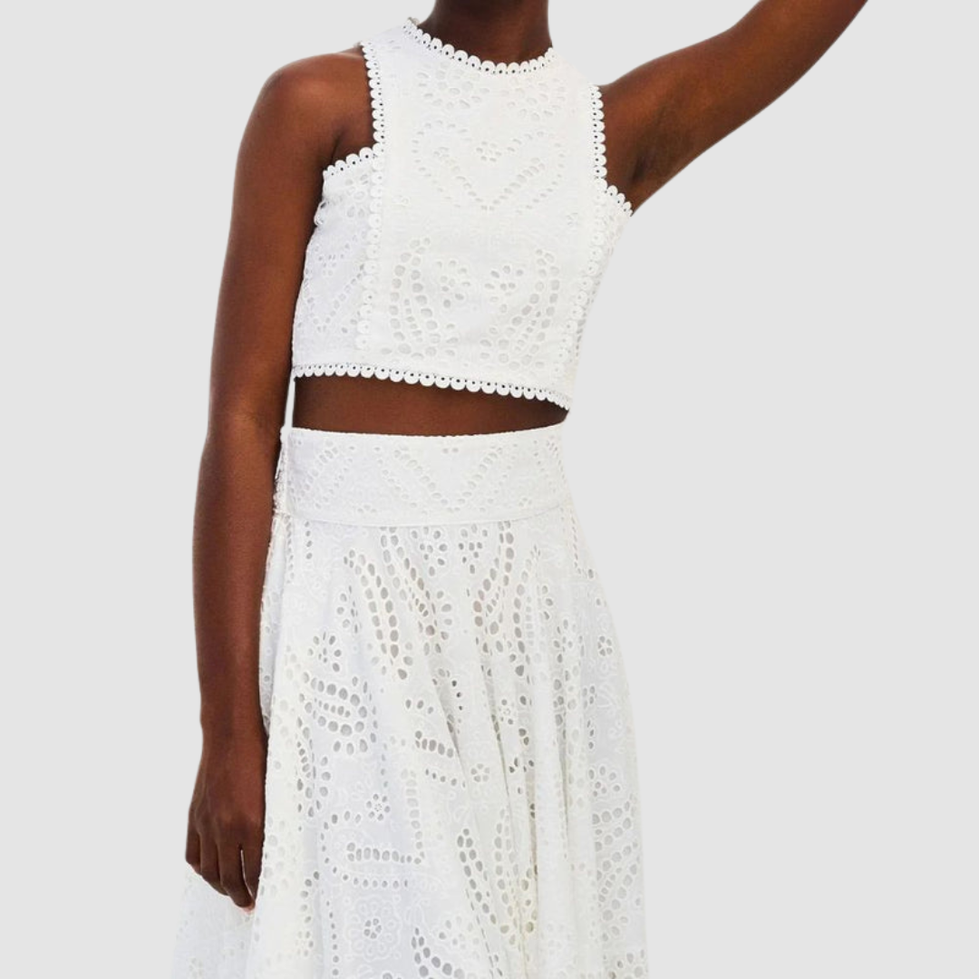 Close-up of a white two-piece set with cutout details, worn by a woman, showing top and waist of skirt on a white backdrop.